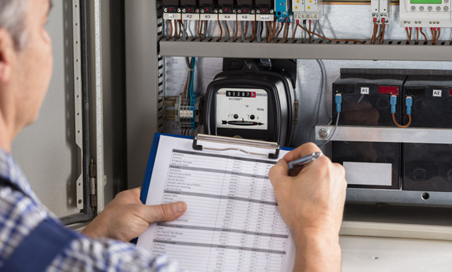 Bei der Überprüfung eines offenen Schaltschranks erfasst eine Person mit dem e-mobilio Selbst-Installations-Check Daten auf einer Checkliste für eine sichere und genaue Installationsprüfung.