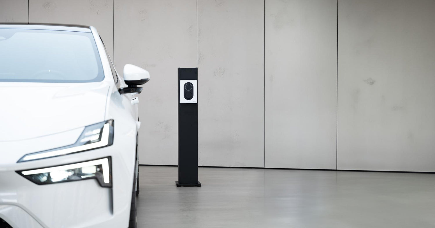 Ein weißes Elektroauto steht in einem Innenbereich neben einer schwarz-weißen Ladestation vor einer schlichten beigen Wand.