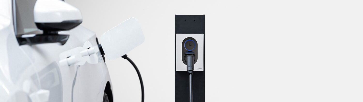 Ein weißes Elektrofahrzeug ist vor einem schlichten weißen Hintergrund an eine schwarz-weiße Ladestation angeschlossen.