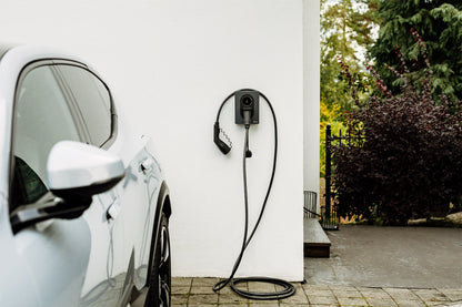 Auf einer gepflasterten Auffahrt parkt ein weißes Elektroauto neben einem Zaptec Go 2 von Zaptec, einer wandmontierten Ladestation mit darunter aufgewickelten Kabeln.